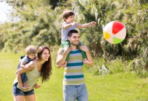Family of four playing with ball in summer park